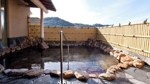 A hot spring bath area with a stone and bamboo fence, a stone wall, and a view of hills in the background. - Sansuien (Kochi)