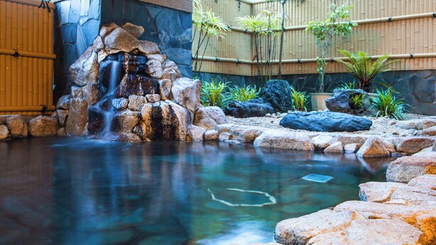 A tranquil indoor garden with a small waterfall, stone rocks, and bamboo plants. - Sansuien (Kochi)