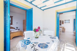 A room with a bed, a table with a vase of flowers, and a chair. - Arhontiko Hotel (Karpathos)