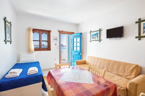 Una habitación con cama, una mesa con mantel, un sofá, un televisor y una ventana con cortinas.