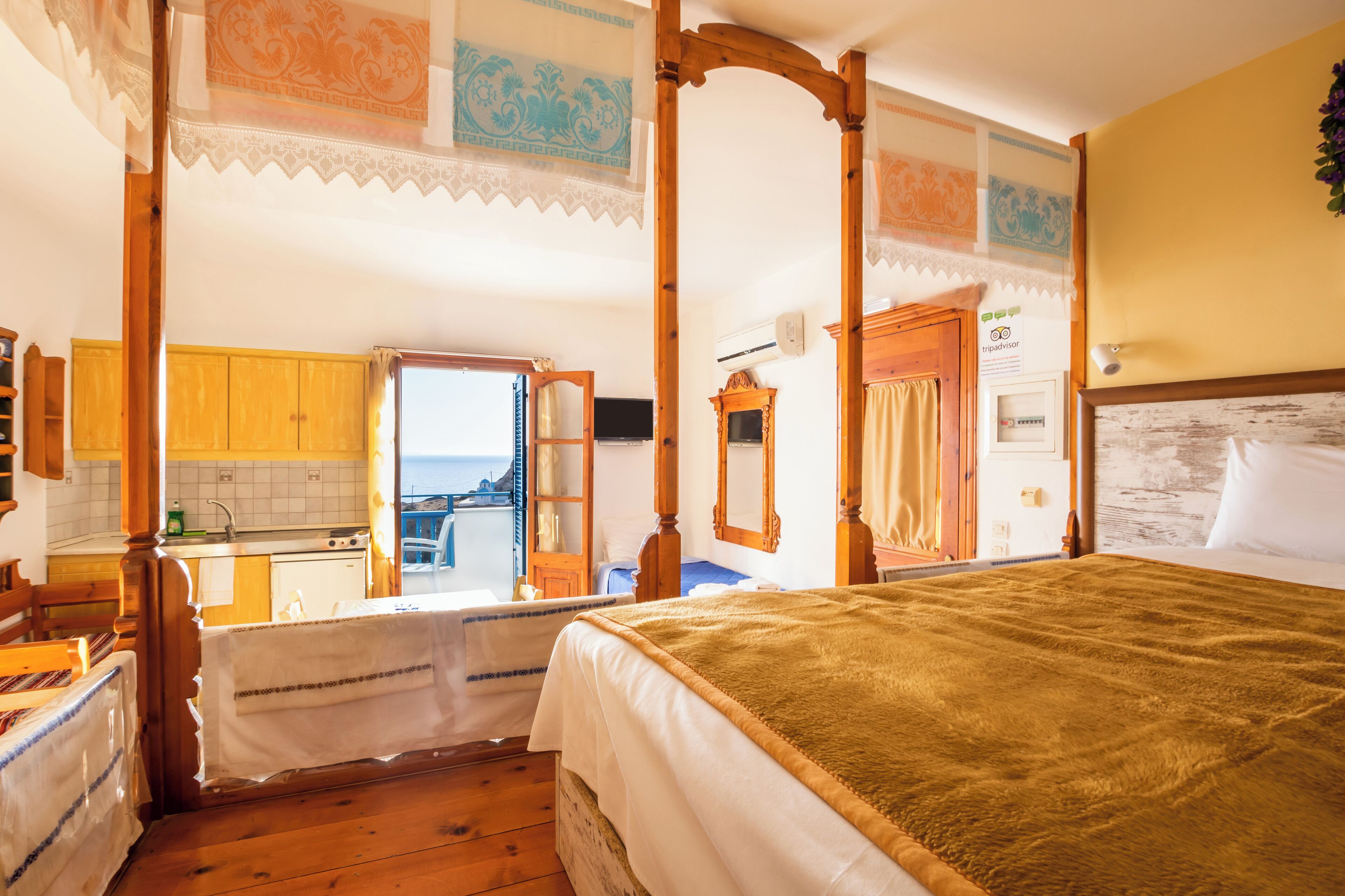 A room with a large bed, wooden furniture, a view of the sea, and a kitchen area.