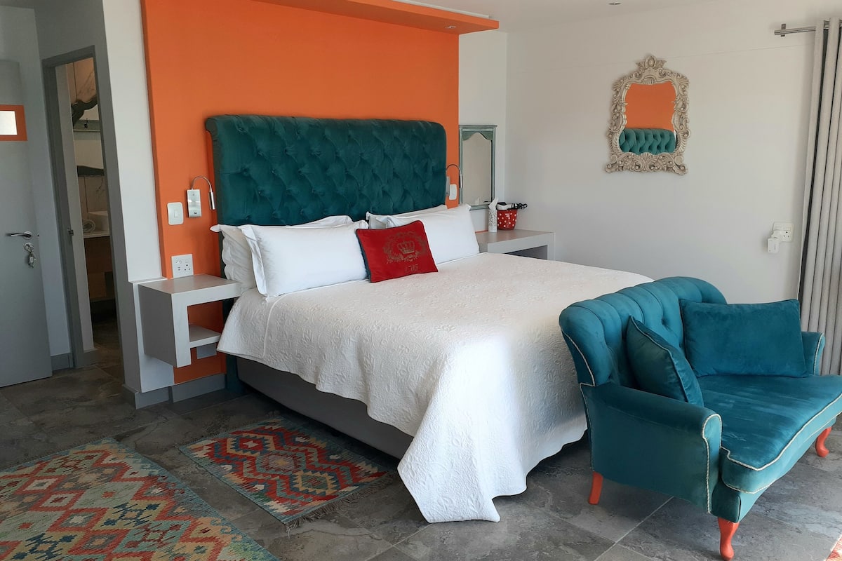A modern bedroom with a teal upholstered headboard, white bedding, and a teal armchair.
