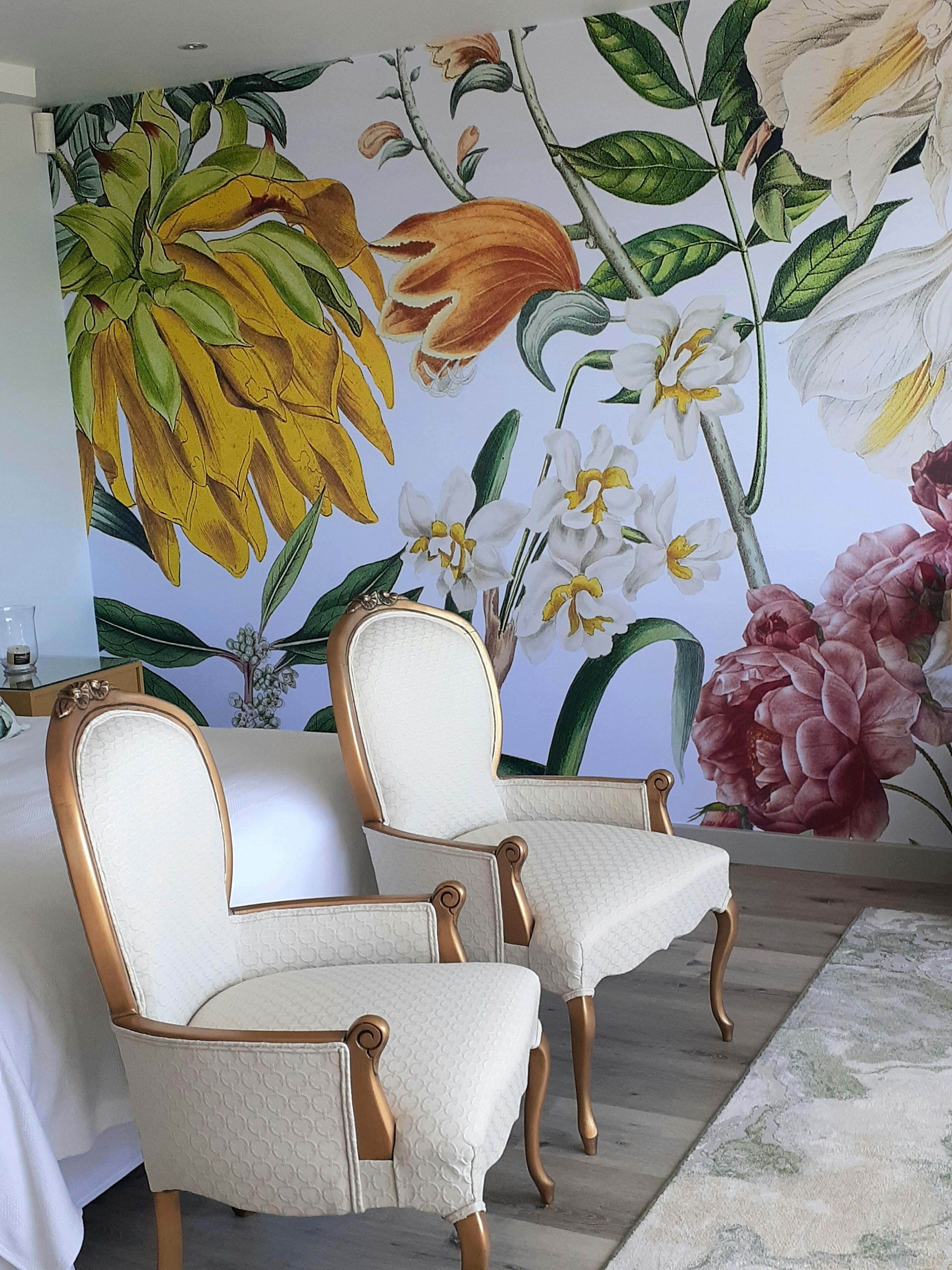A room with two upholstered chairs, a floral mural on the wall, and a wooden floor.