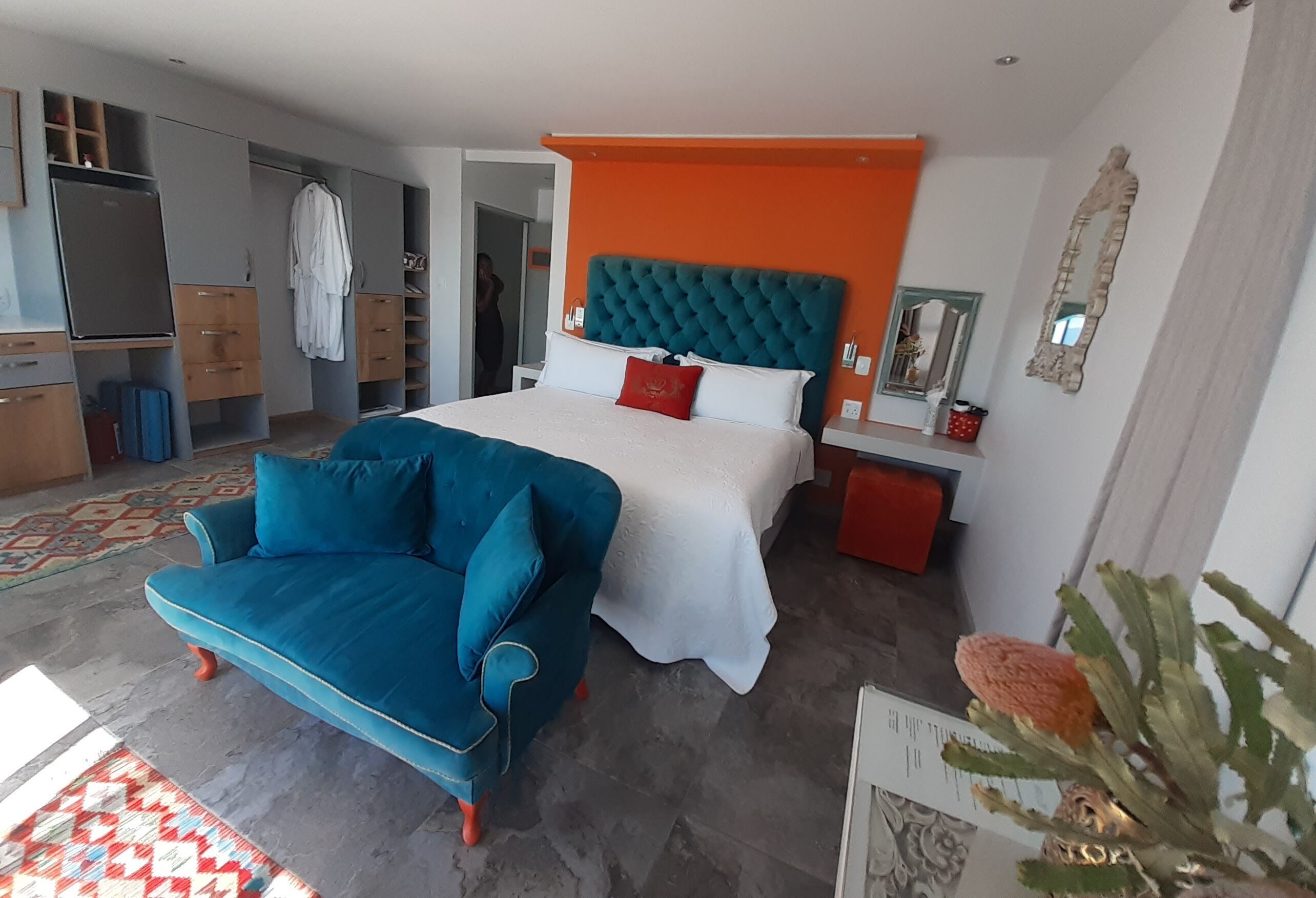 A bedroom with a bed, a blue sofa, a wardrobe, and a mirror.