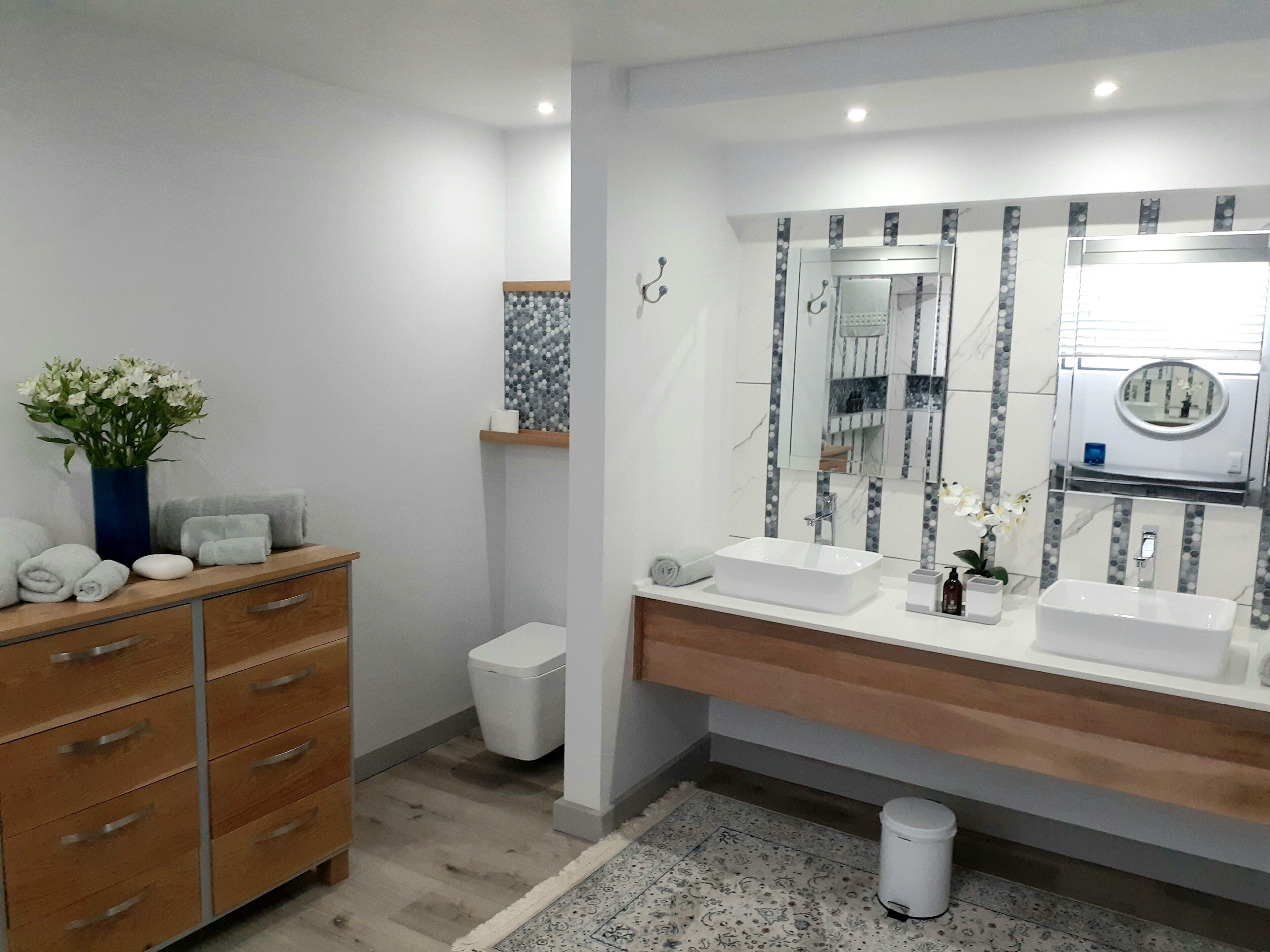 Ein modernes Badezimmer mit zwei Waschbecken, einem großen Spiegel und einer Holzkosmetikbank mit Schubladen.