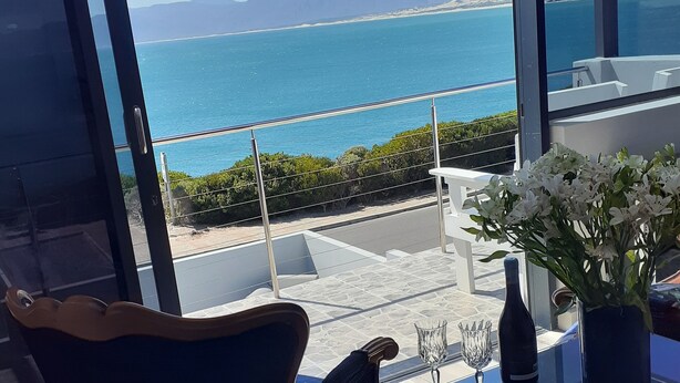 Een kamer met uitzicht op zee, een stoel, een tafel met een bloevas en een fles wijn.