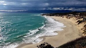 Een strand met golven die op het strand breken, een heldere lucht en bergen in de verte.