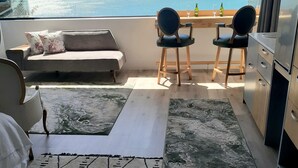 Een balkon met een bank, twee stoelen, een kleine tafel en uitzicht op zee.