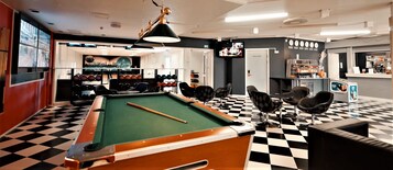 Una sala de billar con mesa de pool, sillas y zona de bar con televisor.