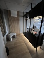 Una habitación de hotel moderna con piso de madera, una banca, un escritorio negro con una bandeja de objetos y un sofá blanco.