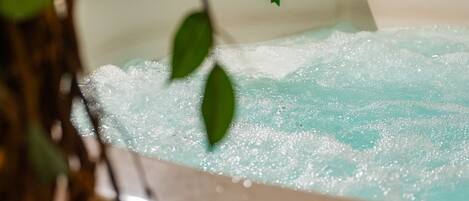 A bathtub with a plant inside, surrounded by a tiled wall and wooden blinds.