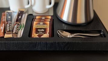 Una estación de café con una cafetera de acero inoxidable, dos tazas blancas, una cuchara y varios pods de café.