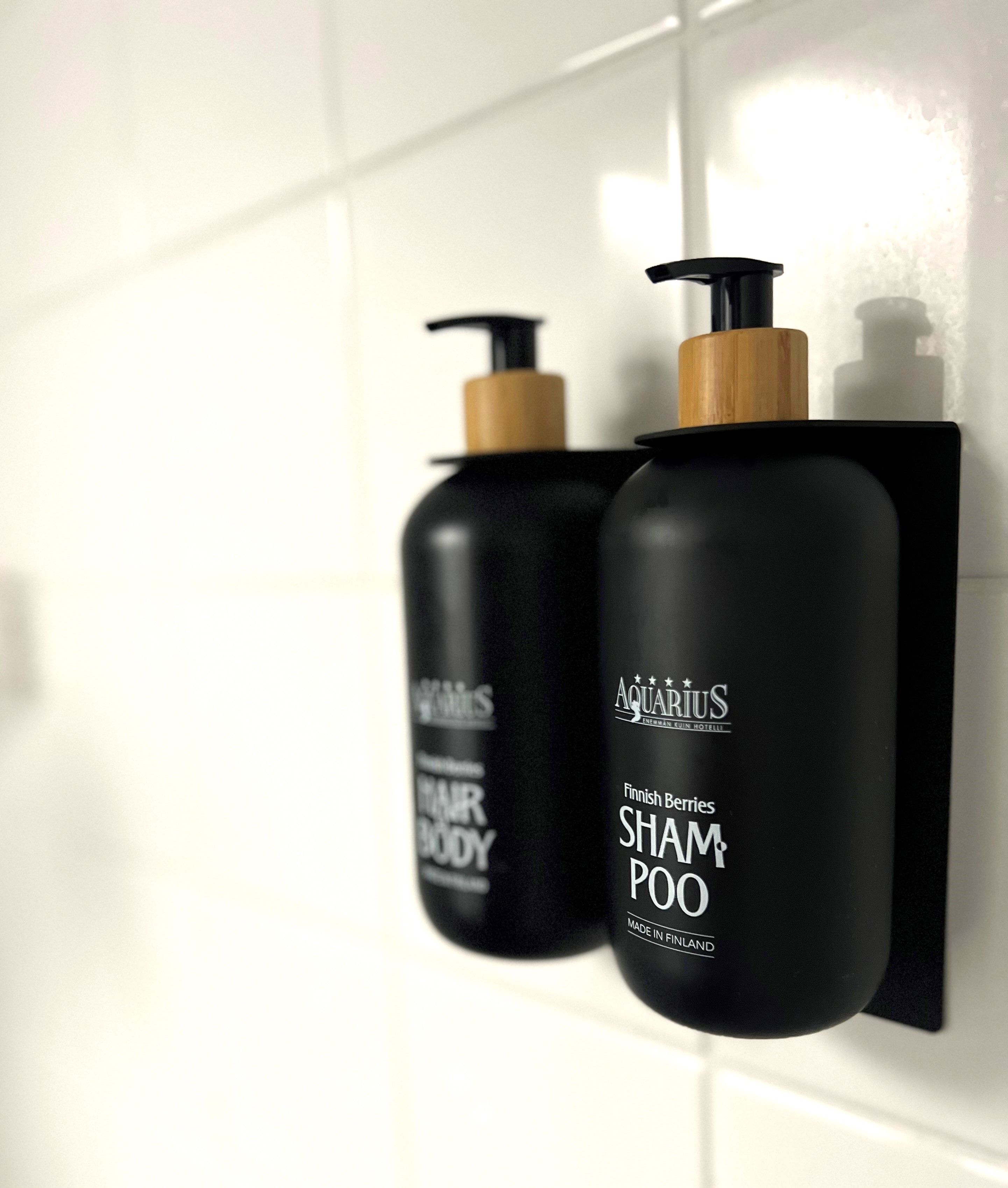 Two black bottles of shampoo and body wash with pumps, labeled 'Aquarius,' mounted on a white tiled wall.