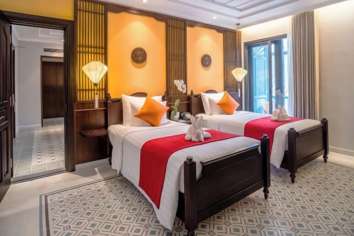 A hotel room with two beds, a mirror, a window, and a patterned floor.