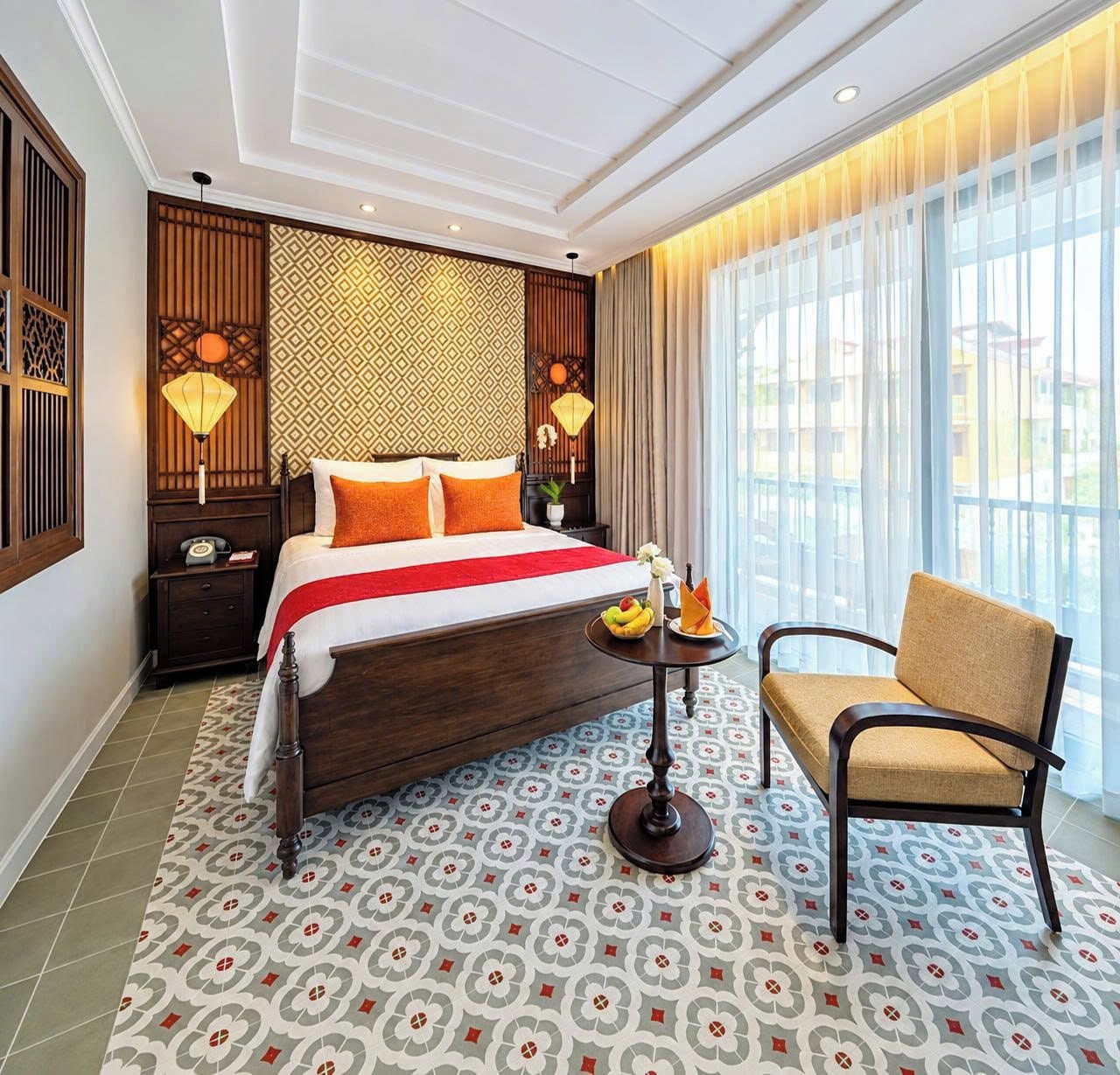 A hotel room with a large bed, a chair, a small table with fruit, and a view of the outside.