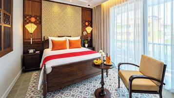A hotel room with a large bed, a chair, a small table with fruit, and a view of the outside.