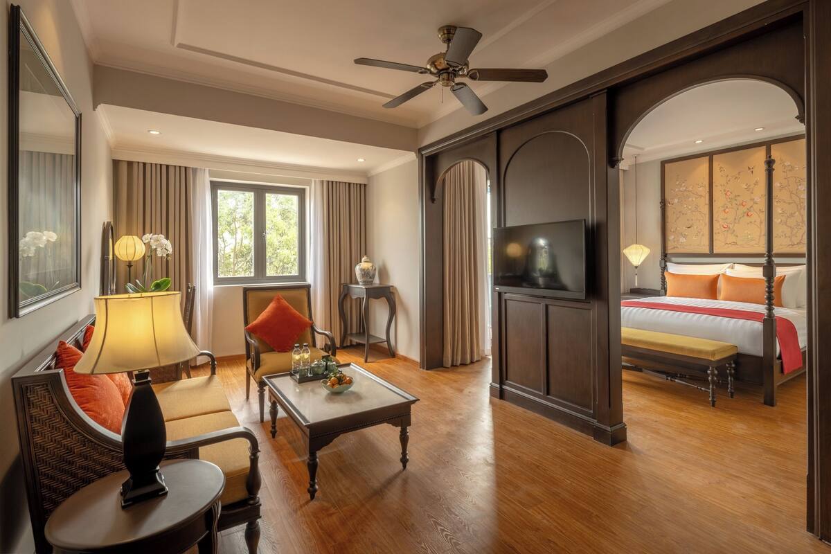 A hotel room with a large bed, a TV, a ceiling fan, a seating area with a table, and a view of the outdoors.