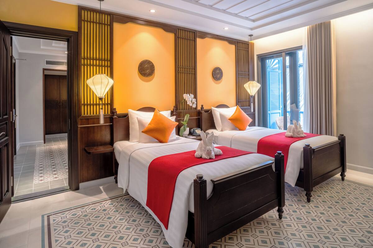 A hotel room with two beds, a wooden headboard, a red throw blanket, and a decorative wall piece.