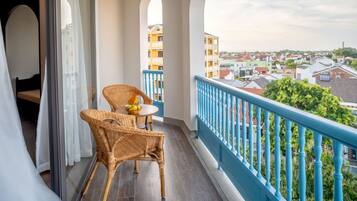 A balcony with wicker chairs and a table, a blue railing, and a view of buildings in the distance.