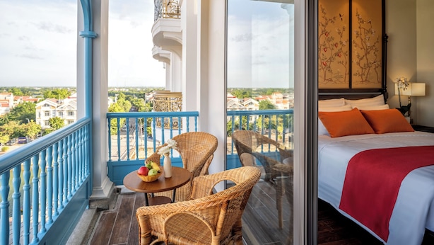A balcony with wicker furniture, a table with fruit, and a bed with orange pillows. - Little Residence. A Boutique Hotel & Spa (Da Nang)