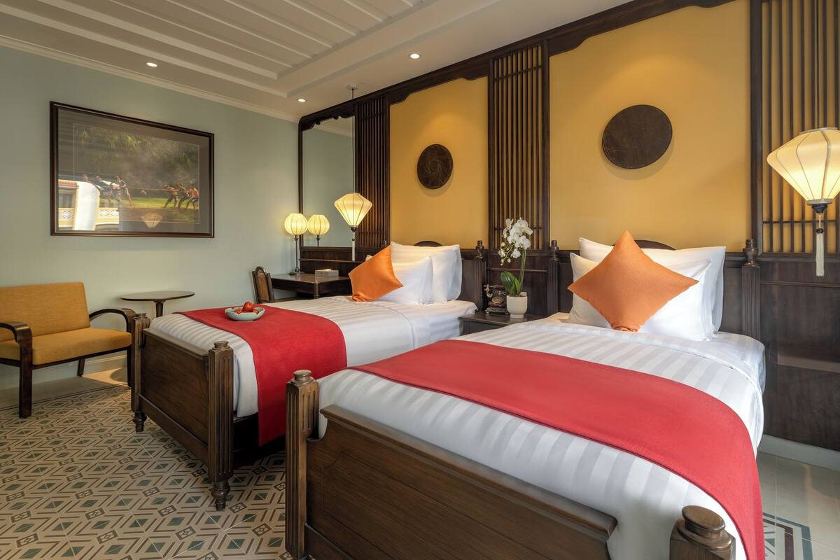 A hotel room with two beds, a small table, a chair, and a large mirror.