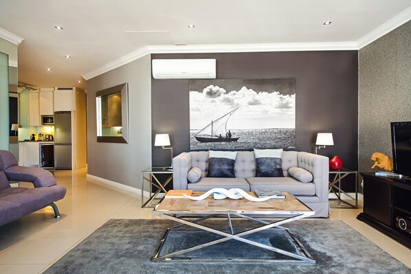 A modern living room with a grey sofa, a coffee table, and a large wall-mounted TV. - 512 The Granger (Cape Town)