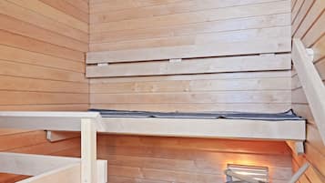A wooden sauna with a bench, a bucket, and two bottles on the floor.