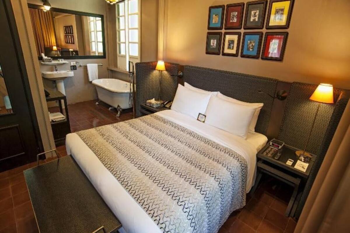 A hotel room with a bed, bedside tables, a nightstand, a bathroom with a bathtub, a sink, and a mirror.