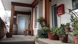 Une véranda en bois avec un banc, des plantes en pot et une porte donnant sur l’intérieur.