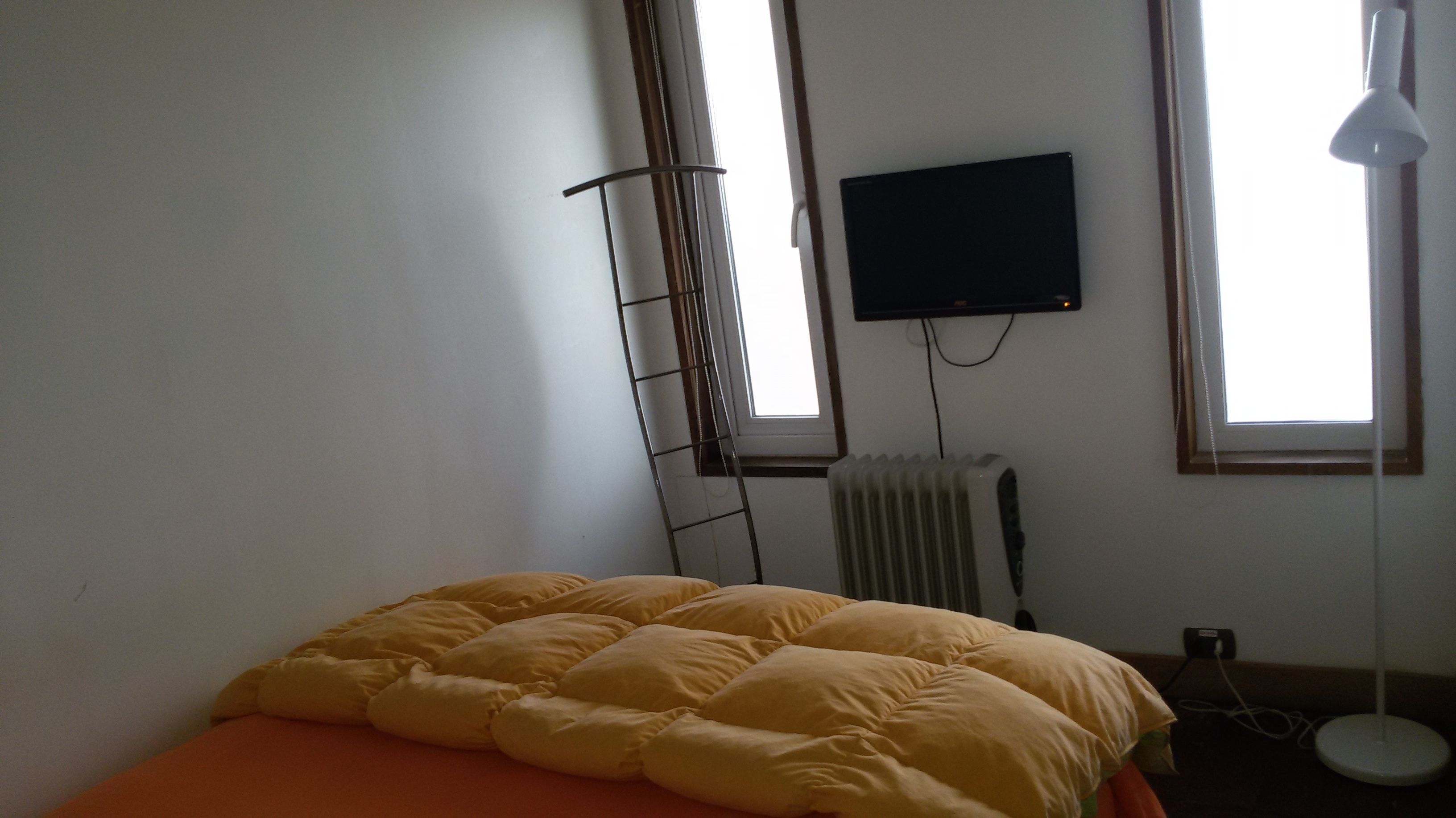 A room with a bed, a radiator, a TV mounted on the wall, and a window with a view.