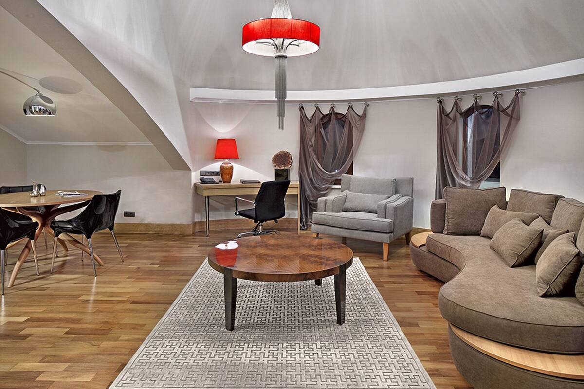 Un vaste salon doté d’un haut plafond, d’une table basse ronde en bois, d’un canapé gris, d’un canapé marron et d’un coin repas avec une table et des chaises.