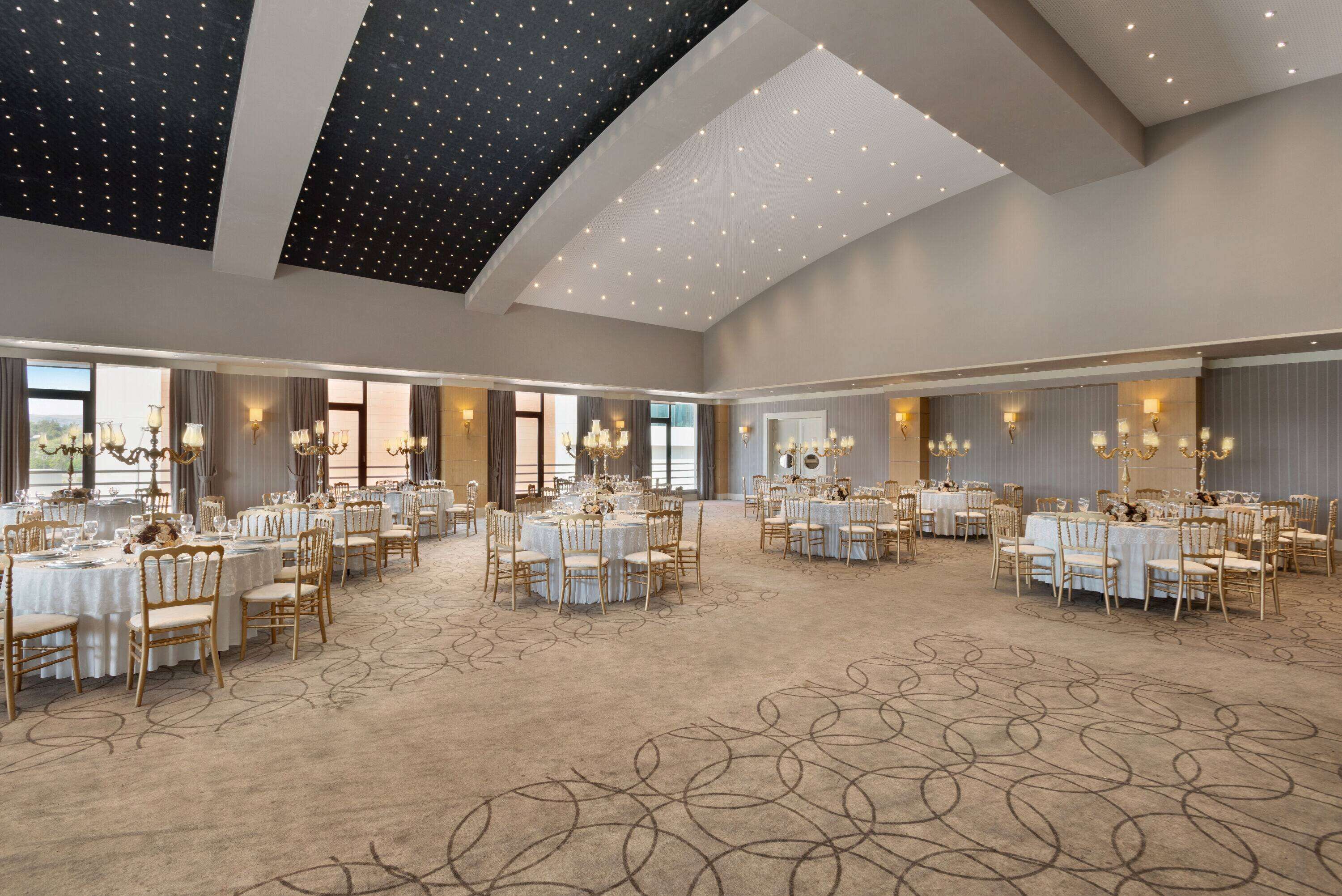Un gran salón de banquetes con mesas redondas, candelabros y piso alfombrado.