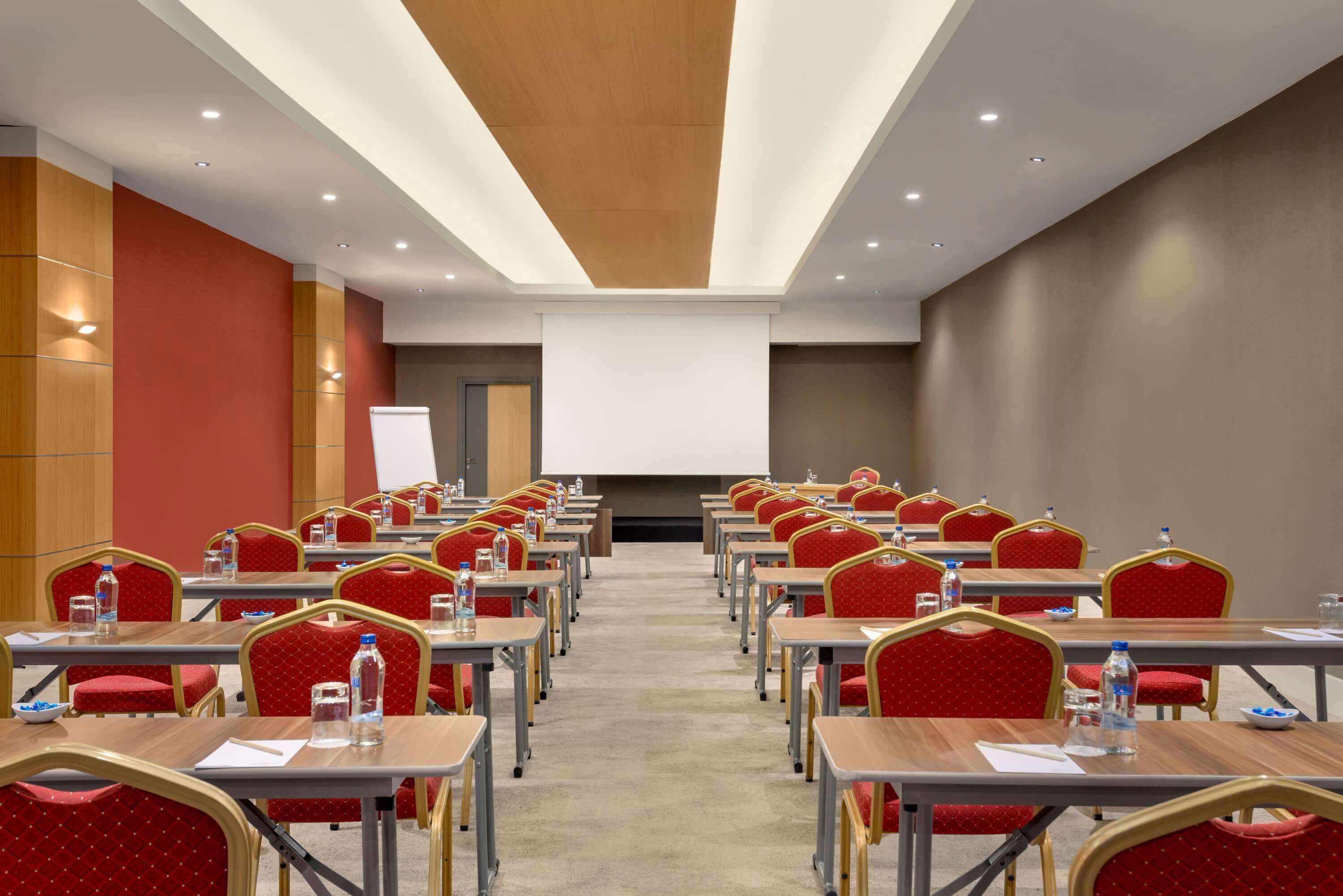 A conference room with rows of tables and chairs, a whiteboard, and a projector screen.