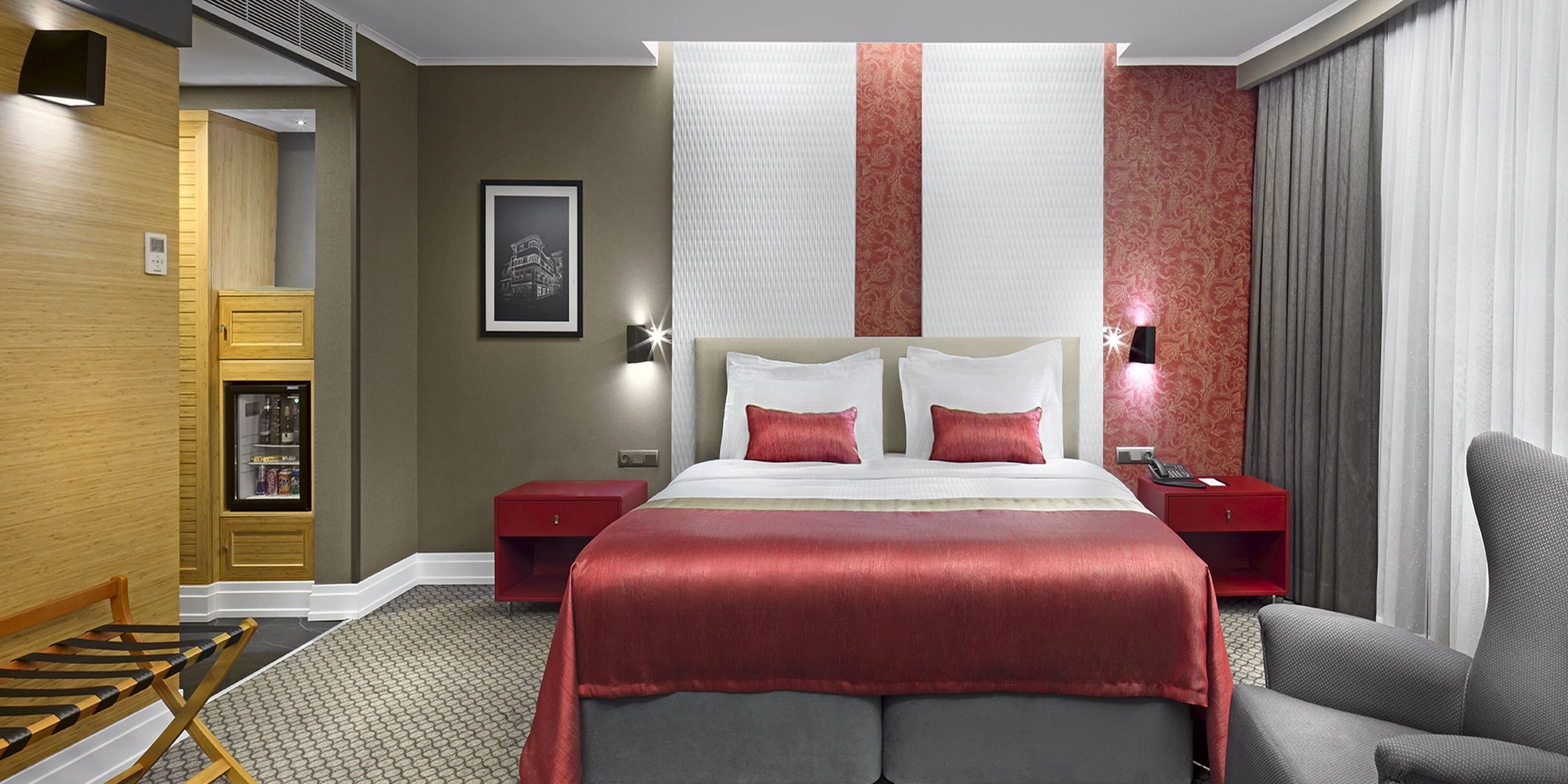 Une chambre d’hôtel avec un grand lit, deux tables de chevet, un rideau rayé rouge et blanc, une armoire en bois et une chaise.