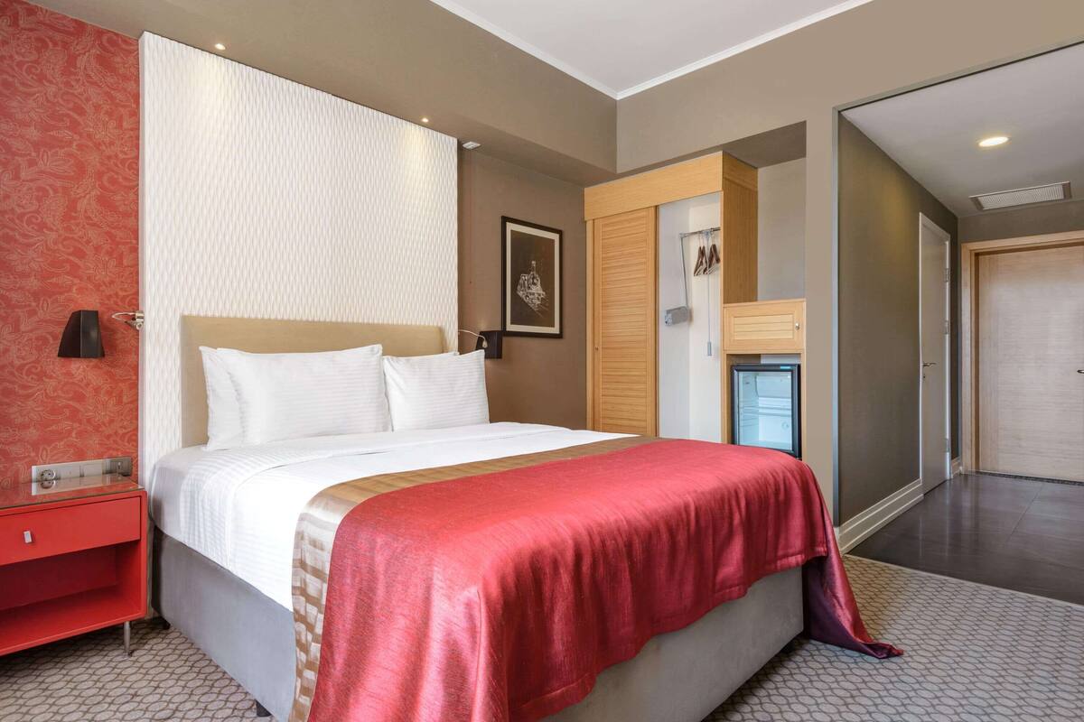 Une chambre d’hôtel avec un lit, une table de chevet, une armoire et une salle de bain visible à travers une porte ouverte.