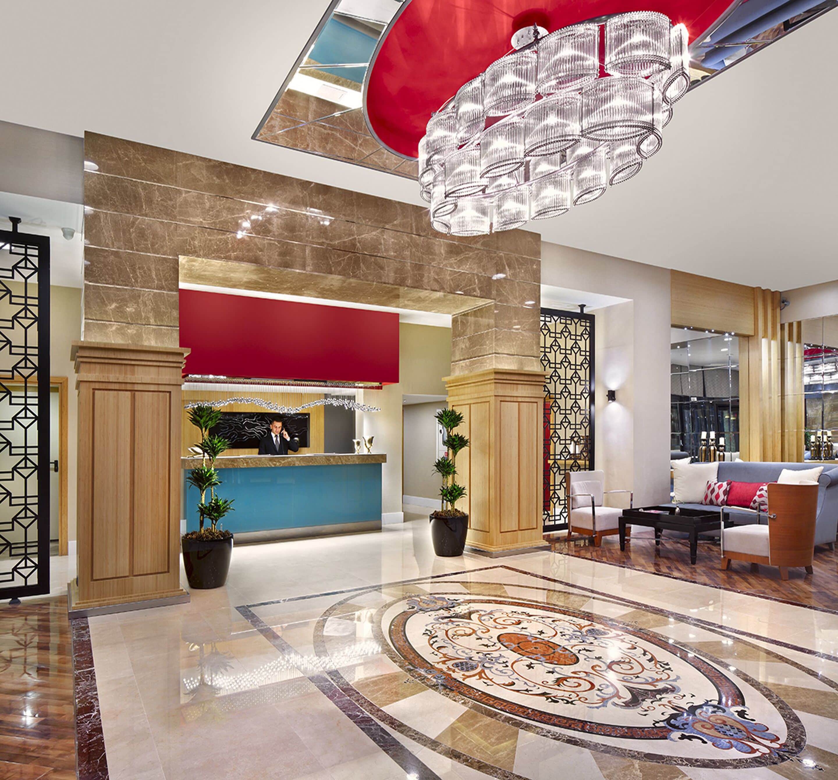Un vestíbulo de hotel con una recepción, una araña, piso estampado y una zona de estar con un sofá y sillones.