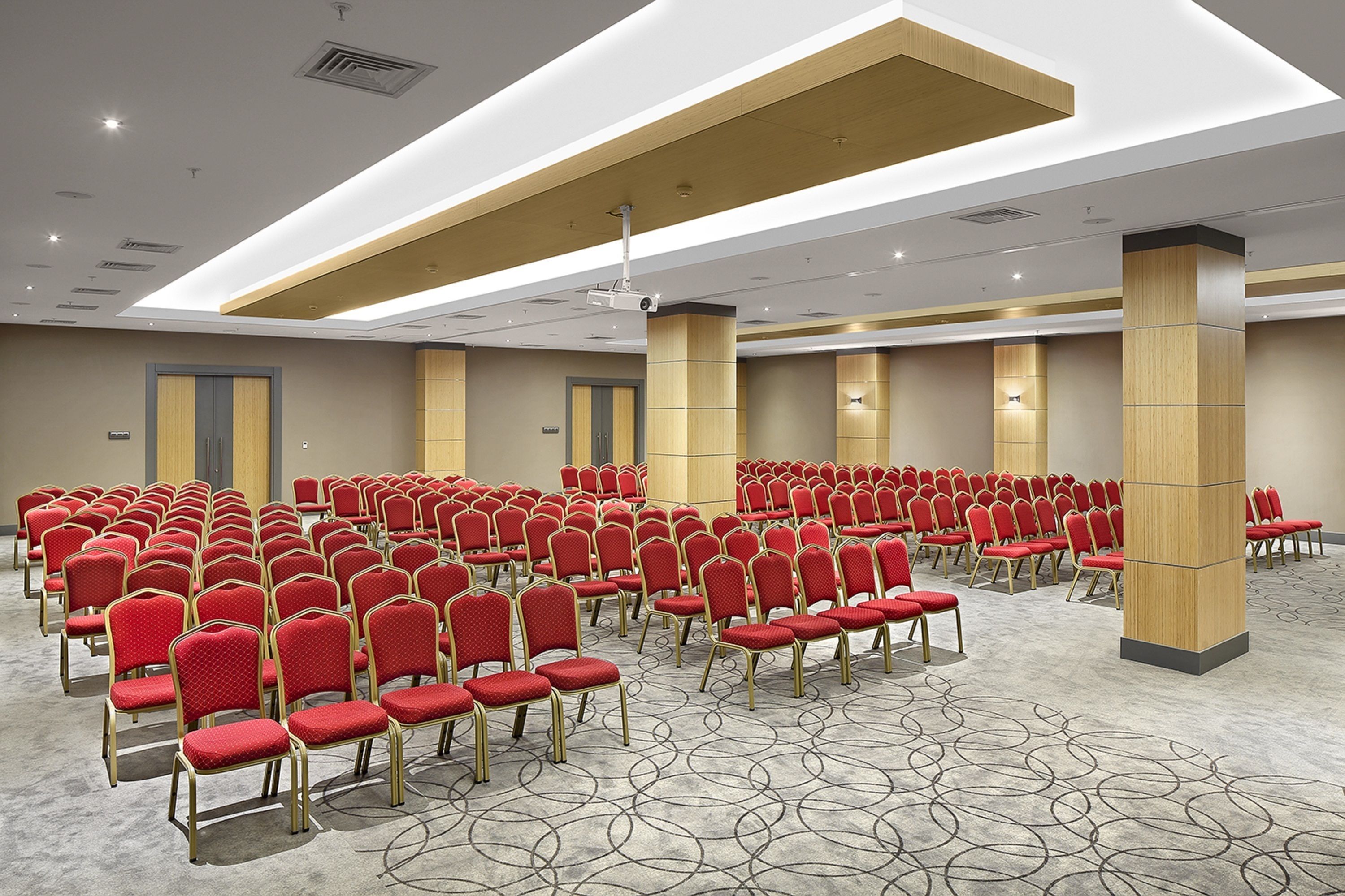 A conference room with rows of red chairs, wooden pillars, and a patterned carpet.