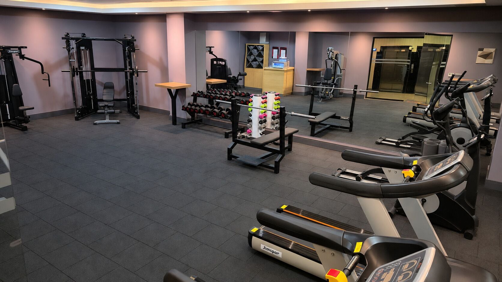 A gym with cardio machines, weightlifting equipment, and dumbbells.