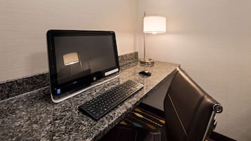 Una computadora portátil sobre una encimera de granito, un teclado, un ratón, una lámpara y una silla de cuero.