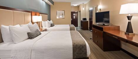 A hotel room with two beds, a desk, a TV, and a lamp.