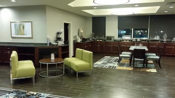 A modern kitchen with dark wood cabinets, a dining area with a table and chairs, and a living area with a sofa and chairs.