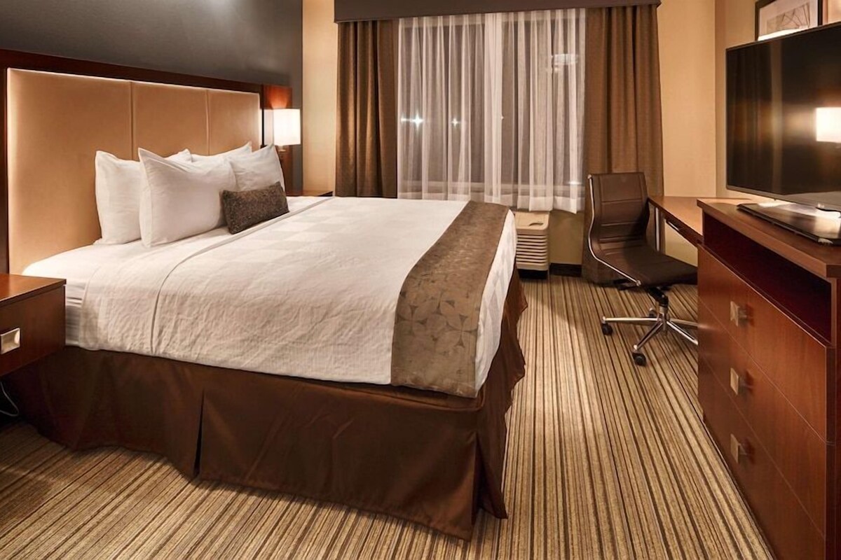 A hotel room with a large bed, a desk with a flat-screen TV, a chair, and a window with curtains.