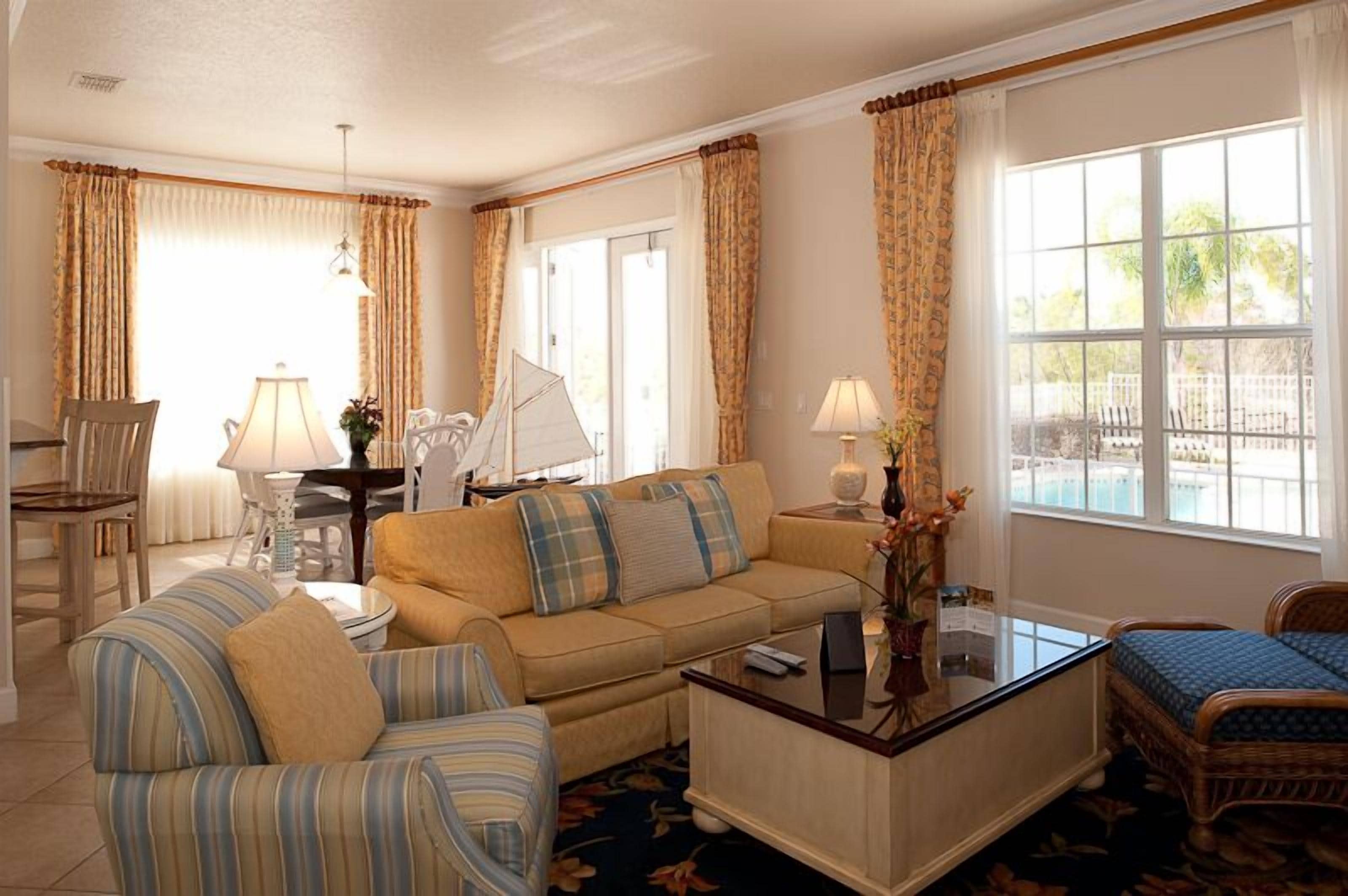 A well-lit living room with a sofa, armchairs, a coffee table, and a dining area with a table and chairs.