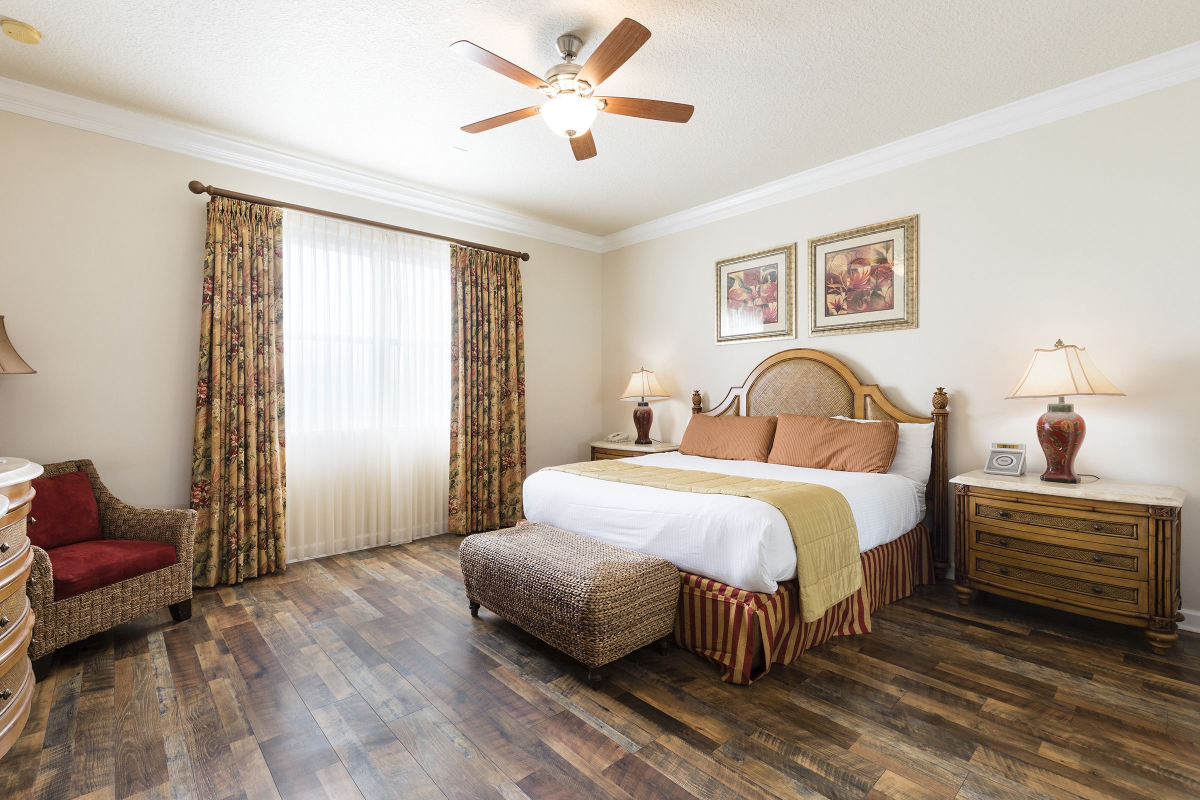 A bedroom with a wooden floor, a bed with a headboard, a nightstand, a chair, and a ceiling fan.