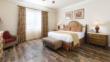 A bedroom with a wooden floor, a bed with a headboard, a nightstand, a chair, and a ceiling fan.