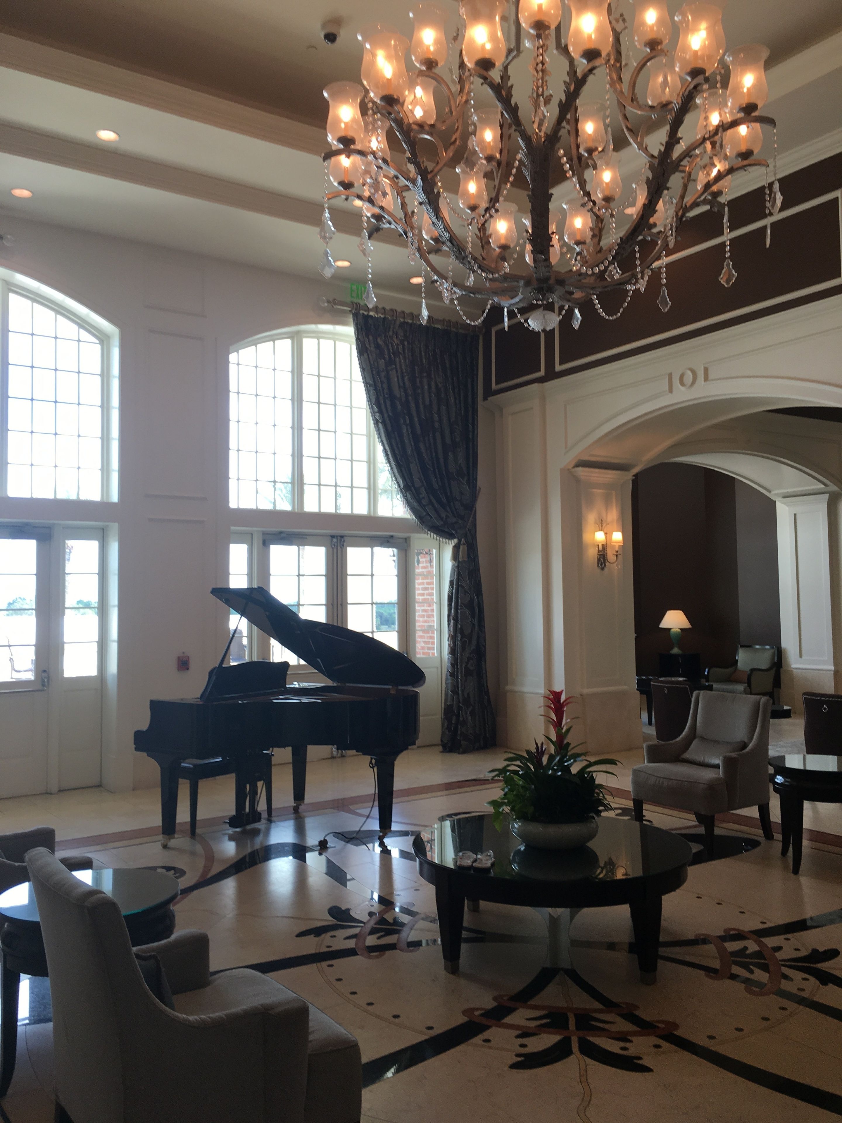 A grand lobby with a grand piano, a chandelier, and a large arched doorway labeled "101".