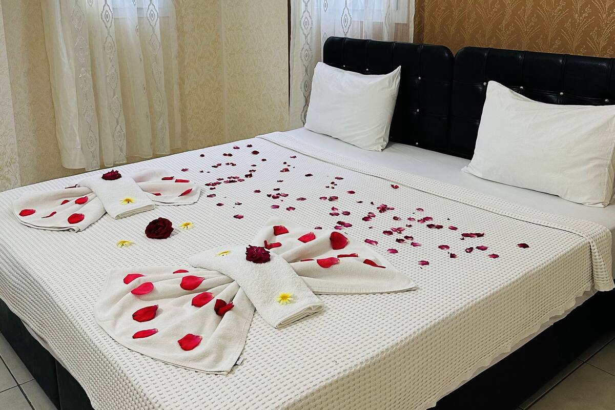 A neatly made bed with a white bedspread and pillows, a black headboard, and a room with beige walls and curtains.