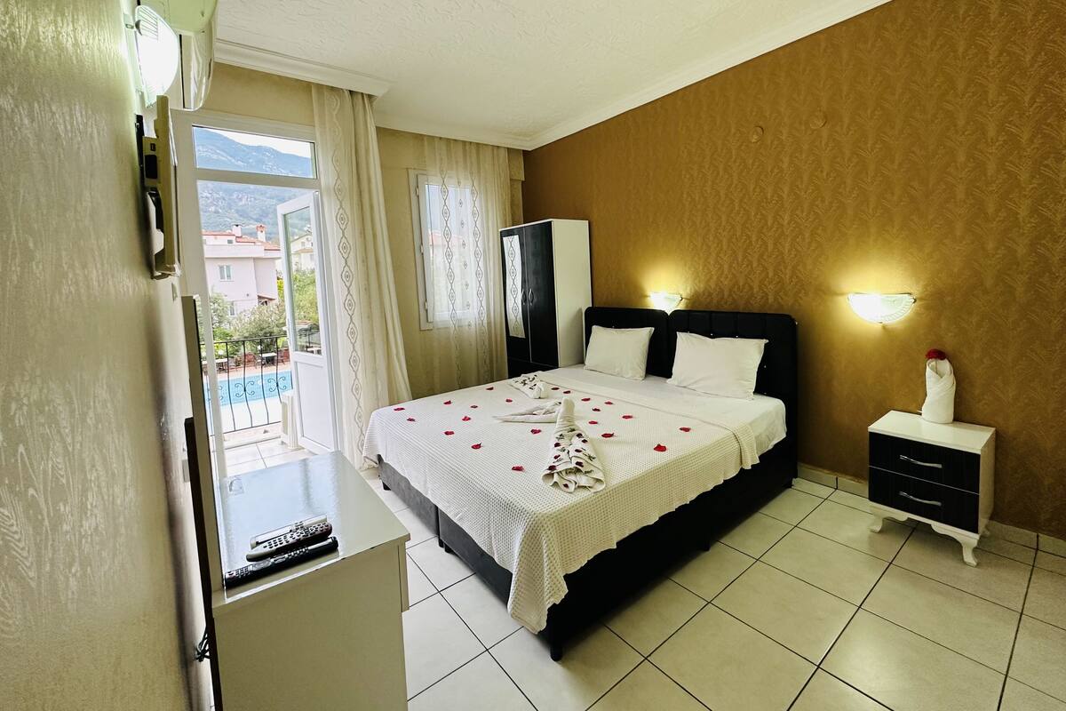 A hotel room with a bed, bedside table, lamp, and a view of the outdoors.