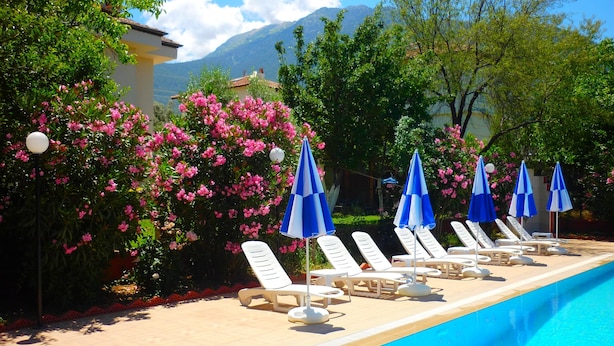 A poolside area with lounge chairs and umbrellas, surrounded by flowering bushes and trees. - The Green Valley Hotel (Fethiye)