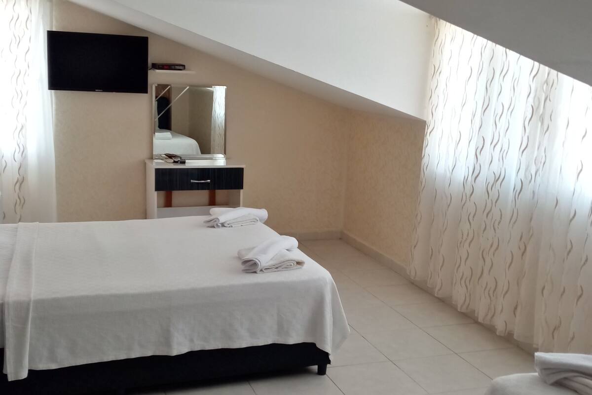 A modern bedroom with a large bed, a small desk, a mirror, and a TV mounted on the wall.